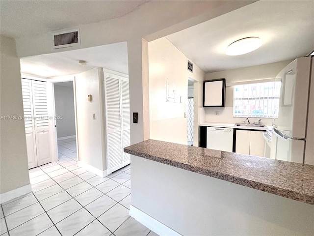 kitchen with light tile patterned flooring, white appliances, sink, and white cabinets