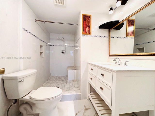 bathroom featuring tiled shower, vanity, toilet, and tile walls