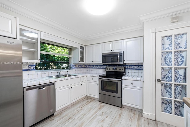 kitchen featuring appliances with stainless steel finishes, sink, white cabinets, ornamental molding, and tile counters