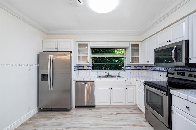 kitchen with appliances with stainless steel finishes, tile countertops, sink, white cabinets, and decorative backsplash