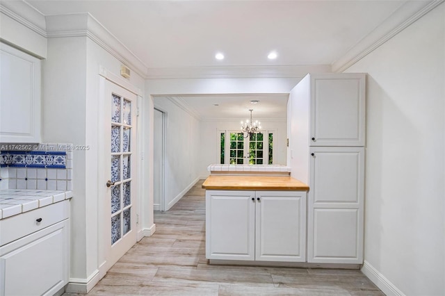 kitchen featuring white cabinetry, hanging light fixtures, ornamental molding, tile counters, and light hardwood / wood-style flooring