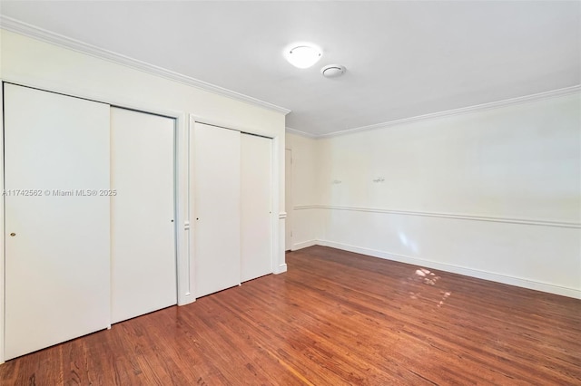 unfurnished bedroom featuring crown molding, hardwood / wood-style floors, and two closets