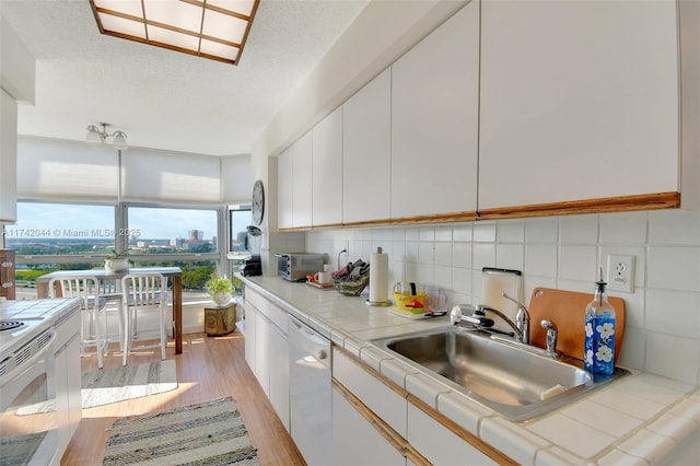 kitchen featuring tile countertops, sink, light wood-type flooring, white cabinets, and white appliances