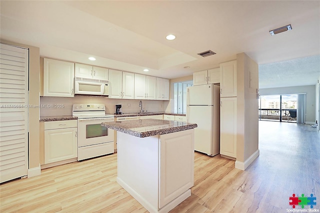 kitchen featuring white appliances, a center island, light hardwood / wood-style floors, white cabinets, and decorative backsplash