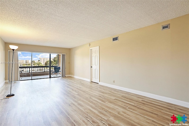 spare room with a textured ceiling, light wood finished floors, visible vents, and baseboards