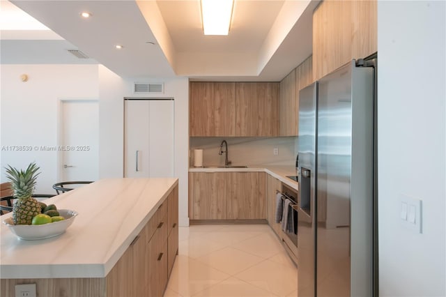 kitchen featuring sink, backsplash, light tile patterned floors, stainless steel fridge with ice dispenser, and a raised ceiling