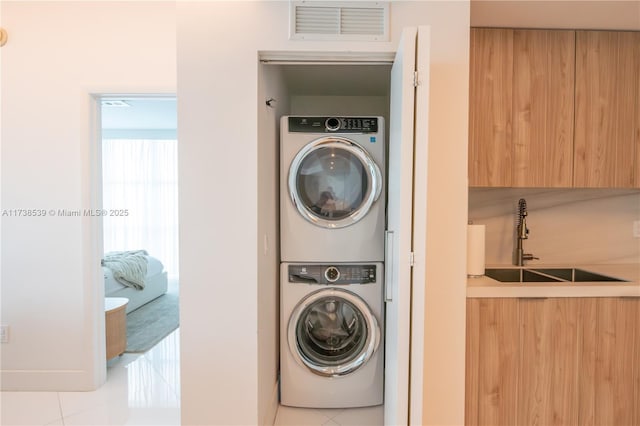 washroom featuring sink, light tile patterned floors, and stacked washing maching and dryer