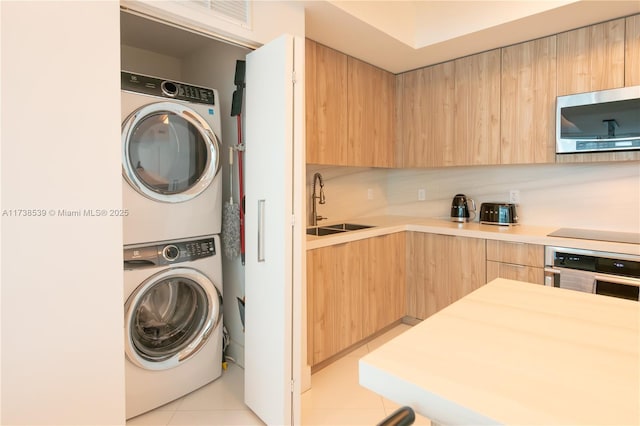 laundry area with sink, light tile patterned flooring, and stacked washer / dryer