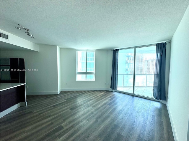 spare room featuring floor to ceiling windows, a healthy amount of sunlight, a textured ceiling, and dark hardwood / wood-style flooring