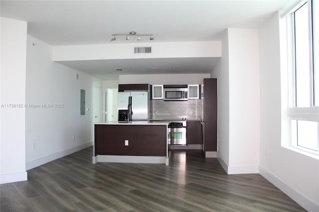 kitchen with appliances with stainless steel finishes, decorative backsplash, electric panel, dark brown cabinetry, and dark wood-type flooring