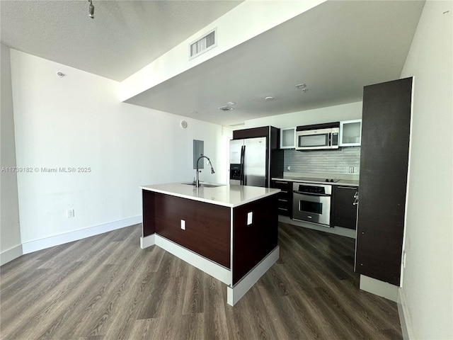 kitchen featuring appliances with stainless steel finishes, sink, backsplash, dark hardwood / wood-style flooring, and a kitchen island with sink