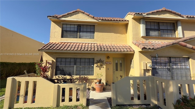 mediterranean / spanish home featuring a tiled roof, a fenced front yard, and stucco siding