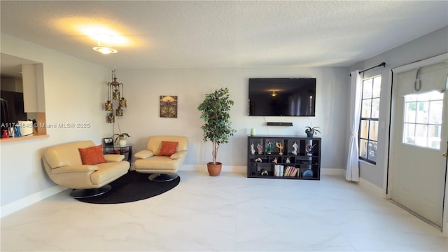 living area featuring marble finish floor, a textured ceiling, and baseboards