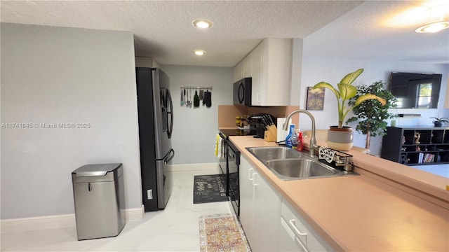 kitchen featuring black microwave, light countertops, freestanding refrigerator, white cabinets, and a sink