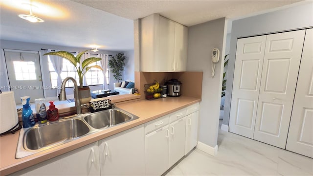 kitchen featuring a sink, light countertops, white cabinets, a textured ceiling, and marble finish floor