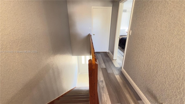 hallway with an upstairs landing, wood finished floors, and a textured wall