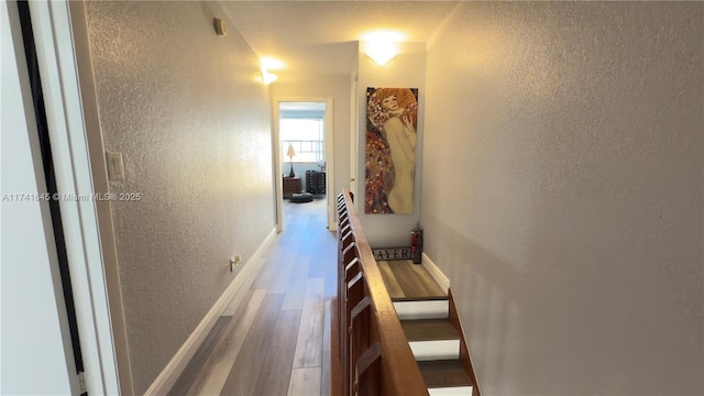 corridor with wood finished floors, a textured wall, and baseboards