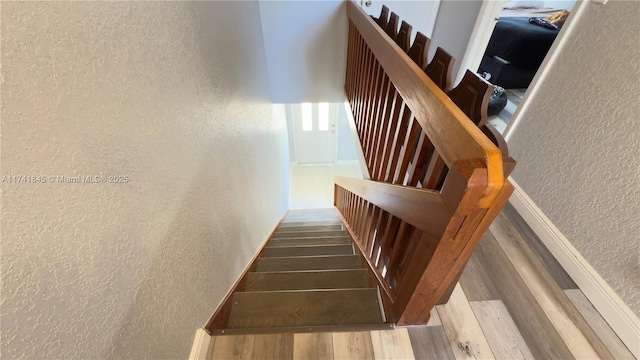 stairs with wood finished floors and a textured wall