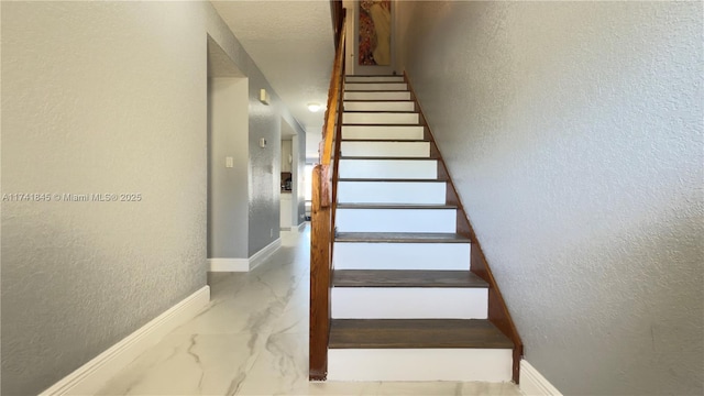 stairway featuring baseboards, marble finish floor, and a textured wall