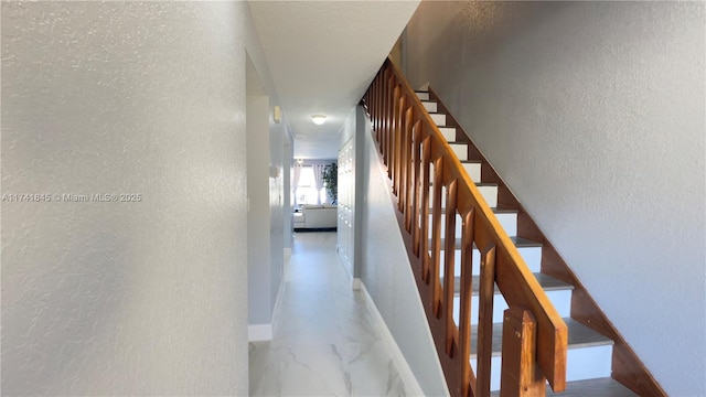 hall featuring stairway, marble finish floor, baseboards, and a textured wall