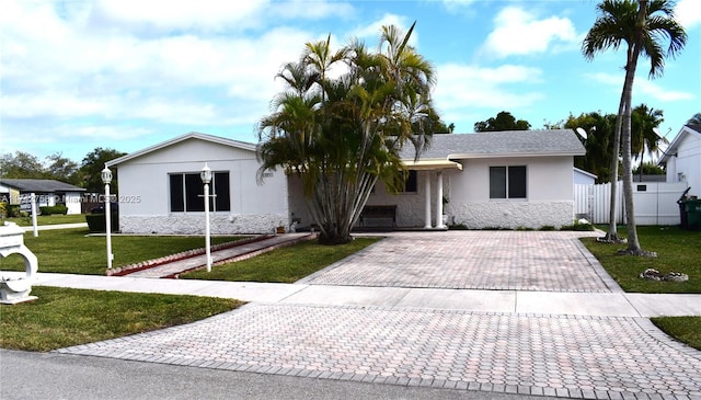 view of front of property featuring fence, stucco siding, a front lawn, stone siding, and decorative driveway