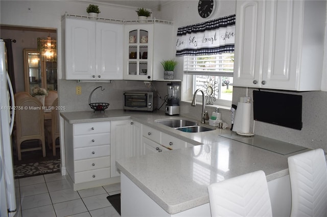 kitchen with a peninsula, a sink, light countertops, glass insert cabinets, and white cabinetry