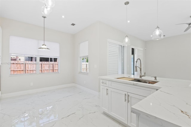 kitchen featuring light stone countertops, sink, white cabinets, and decorative light fixtures