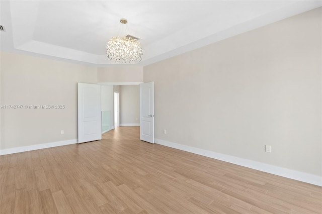 empty room featuring an inviting chandelier, a tray ceiling, and light wood-type flooring