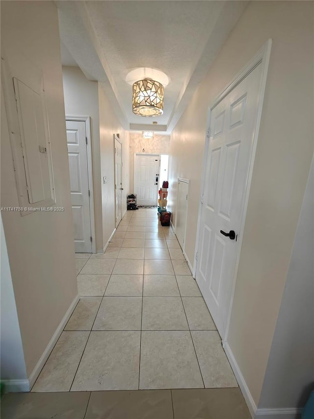 hall with a raised ceiling and light tile patterned floors