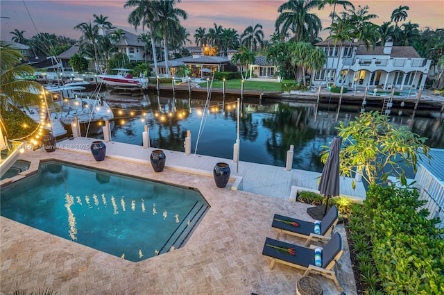 pool at dusk with a water view and a dock