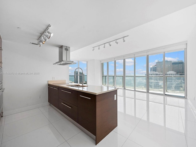 kitchen with a peninsula, island exhaust hood, a sink, dark brown cabinetry, and modern cabinets