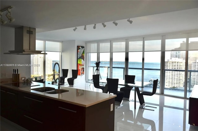 kitchen featuring island range hood, sink, expansive windows, black electric stovetop, and a water view