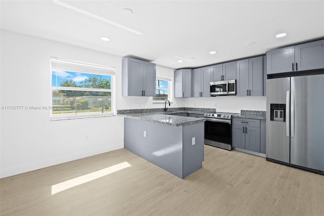 kitchen with gray cabinetry, appliances with stainless steel finishes, light hardwood / wood-style flooring, and dark stone countertops