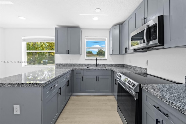 kitchen featuring gray cabinetry, stainless steel appliances, sink, and dark stone counters