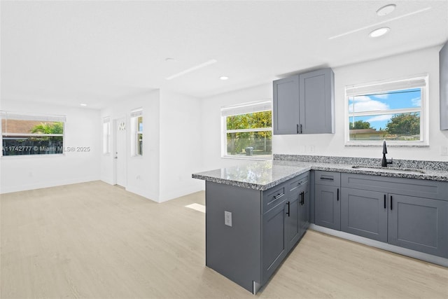 kitchen with gray cabinetry, sink, light hardwood / wood-style floors, and stone counters