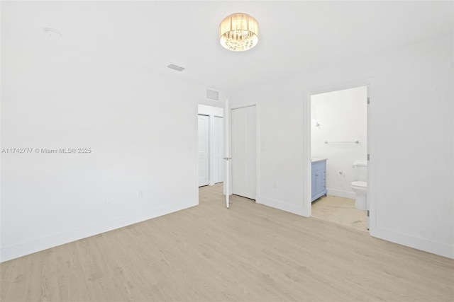 unfurnished bedroom featuring a notable chandelier, ensuite bathroom, and light wood-type flooring