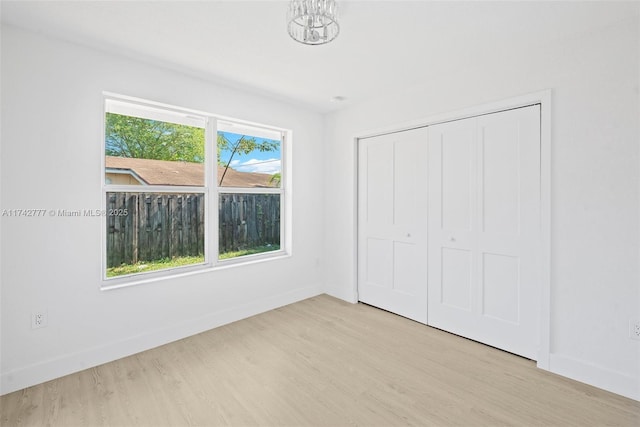 unfurnished bedroom featuring an inviting chandelier, light hardwood / wood-style flooring, and a closet