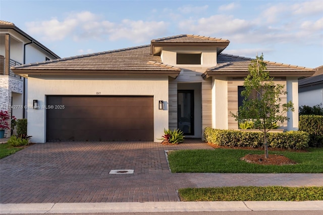 prairie-style home featuring a garage, decorative driveway, and stucco siding