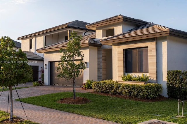 view of front of house featuring a garage, a tile roof, decorative driveway, a front yard, and stucco siding