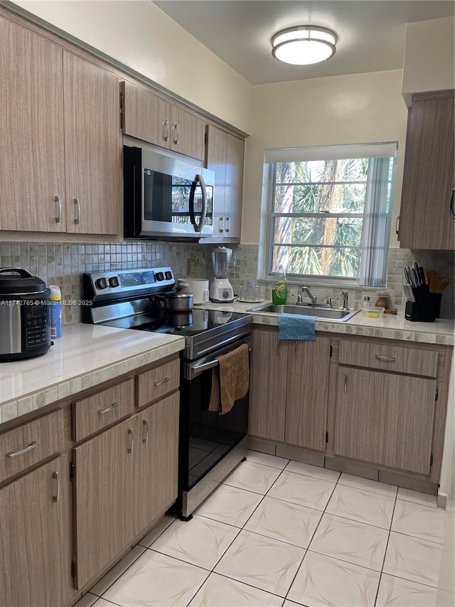 kitchen featuring light countertops, decorative backsplash, appliances with stainless steel finishes, light tile patterned flooring, and a sink