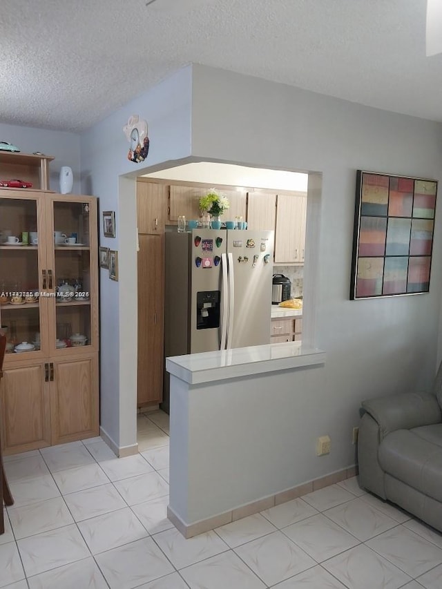 kitchen featuring a textured ceiling, a peninsula, stainless steel fridge with ice dispenser, and light countertops