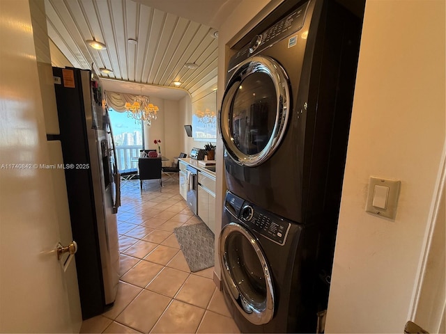 laundry room featuring stacked washer / dryer, light tile patterned flooring, and an inviting chandelier