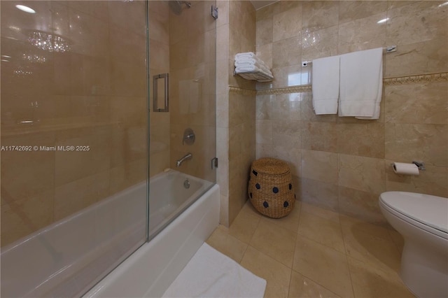 bathroom with tile patterned flooring, combined bath / shower with glass door, tile walls, and toilet