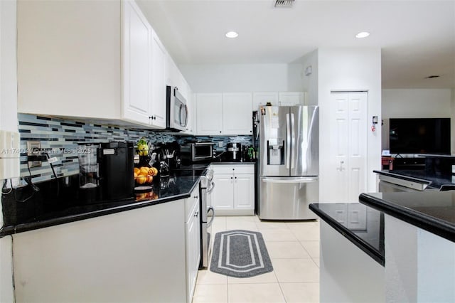 kitchen featuring light tile patterned floors, appliances with stainless steel finishes, white cabinetry, decorative backsplash, and dark stone counters