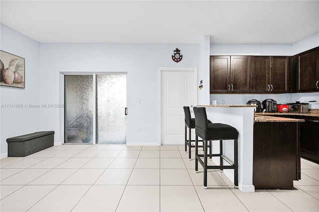 kitchen featuring light tile patterned flooring, dark brown cabinetry, a breakfast bar, and a kitchen island