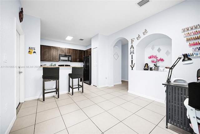 kitchen featuring light tile patterned flooring, dark brown cabinetry, a breakfast bar, and black appliances