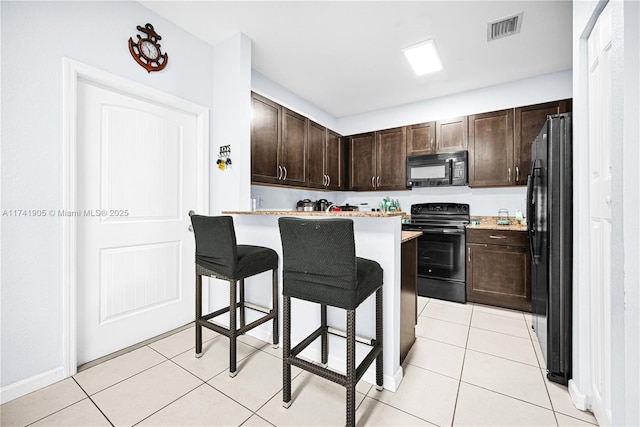 kitchen featuring a kitchen bar, light tile patterned floors, dark brown cabinets, and black appliances