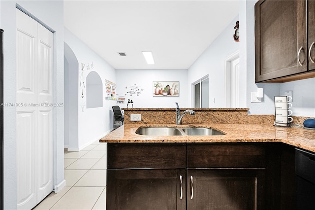 kitchen featuring light tile patterned flooring, dishwasher, sink, light stone counters, and dark brown cabinets