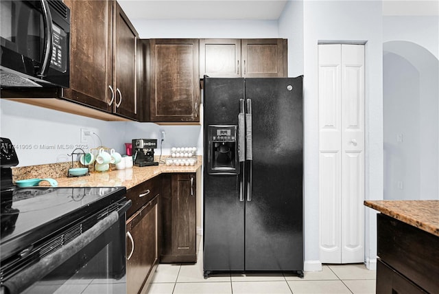 kitchen featuring light stone counters, light tile patterned floors, dark brown cabinets, and black appliances