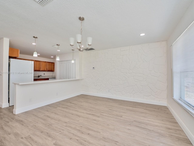 kitchen featuring pendant lighting, light hardwood / wood-style floors, kitchen peninsula, and white fridge